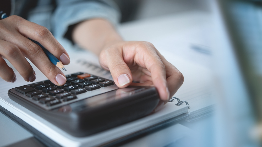 View of a person calculating AC unit installation costs for a home with a calculator and pencil.