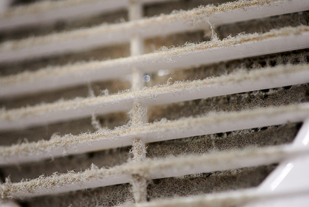 View of a dusty air vent grille with dirt accumulation, emphasizing the importance of regular cleaning.