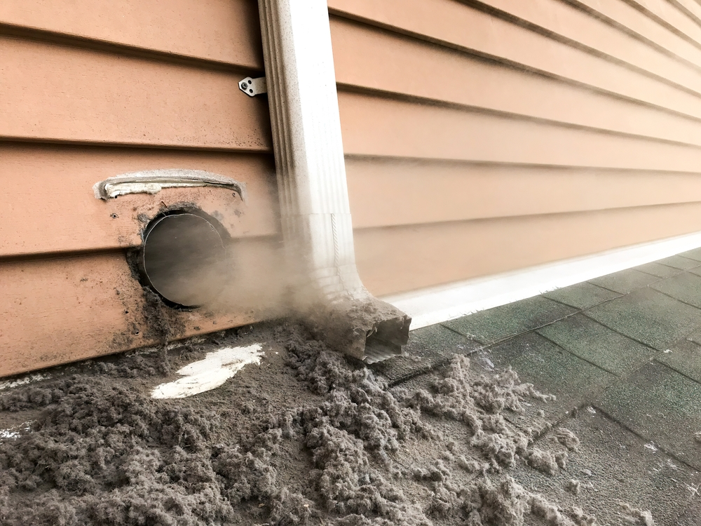 View of a clogged dryer vent expelling lint and dust buildup, indicating a need for cleaning or maintenance.