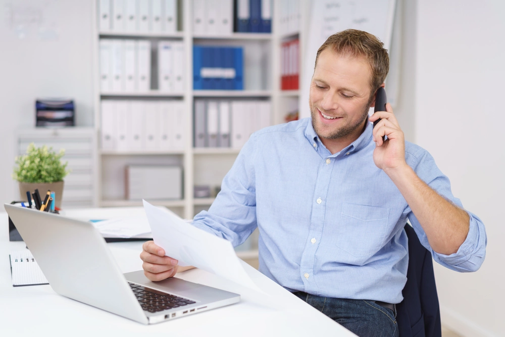 A concentrated man, dressed in a light blue polo, holds a phone conversation.
