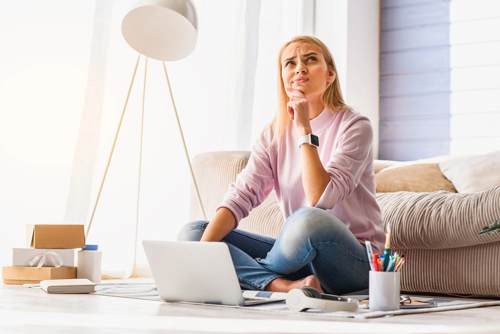 Thinking woman sits in front of laptop.