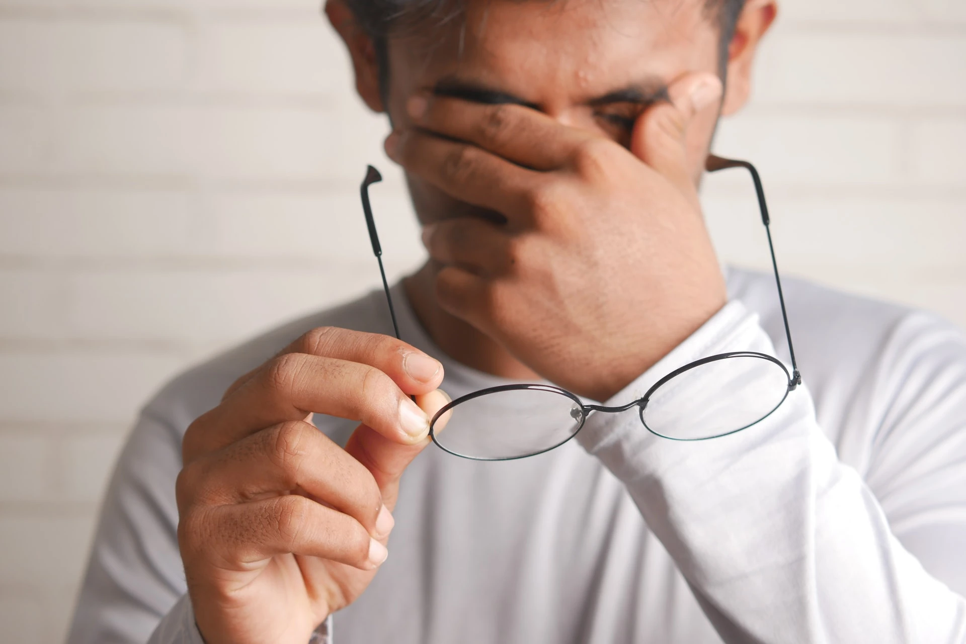 Man with headache takes glasses off of his face.