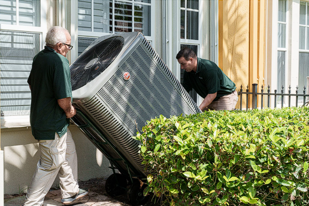 View of technicians transporting an outdoor AC unit during HVAC replacement.