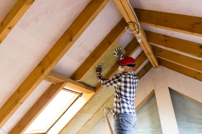 View of a professional carefully laying out the insulation panel on the attic.