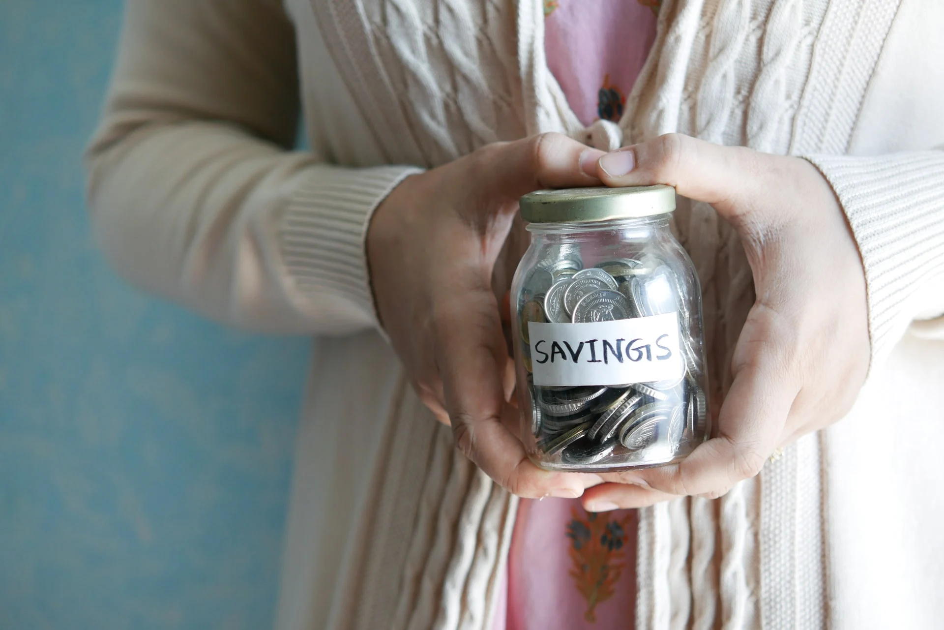 An image of a woman's hand holding a clear jar filled with coins.
