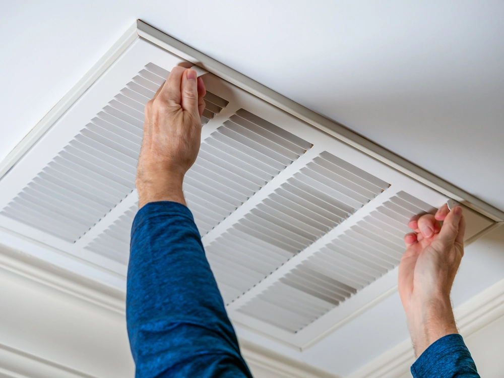 Man opens ceiling air duct vent to change air filter.