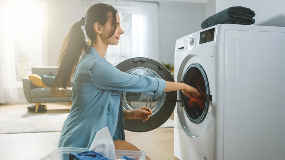 Women loading a white dryer with clothing.