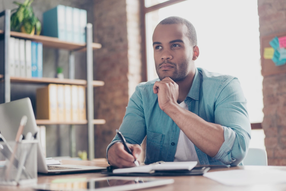 Man at desk thinks while writing notes.