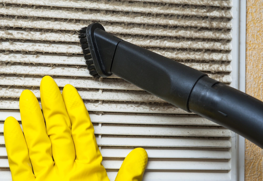 Gloved hand and vacuum clean air vent grill.