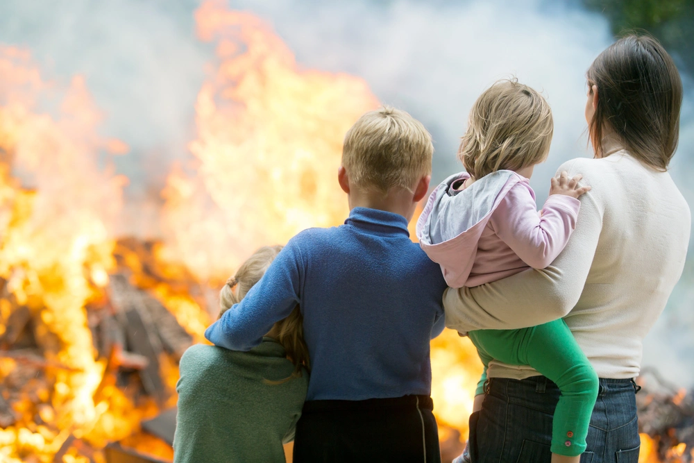 A picture of a mother with her children watching something burning in the background.