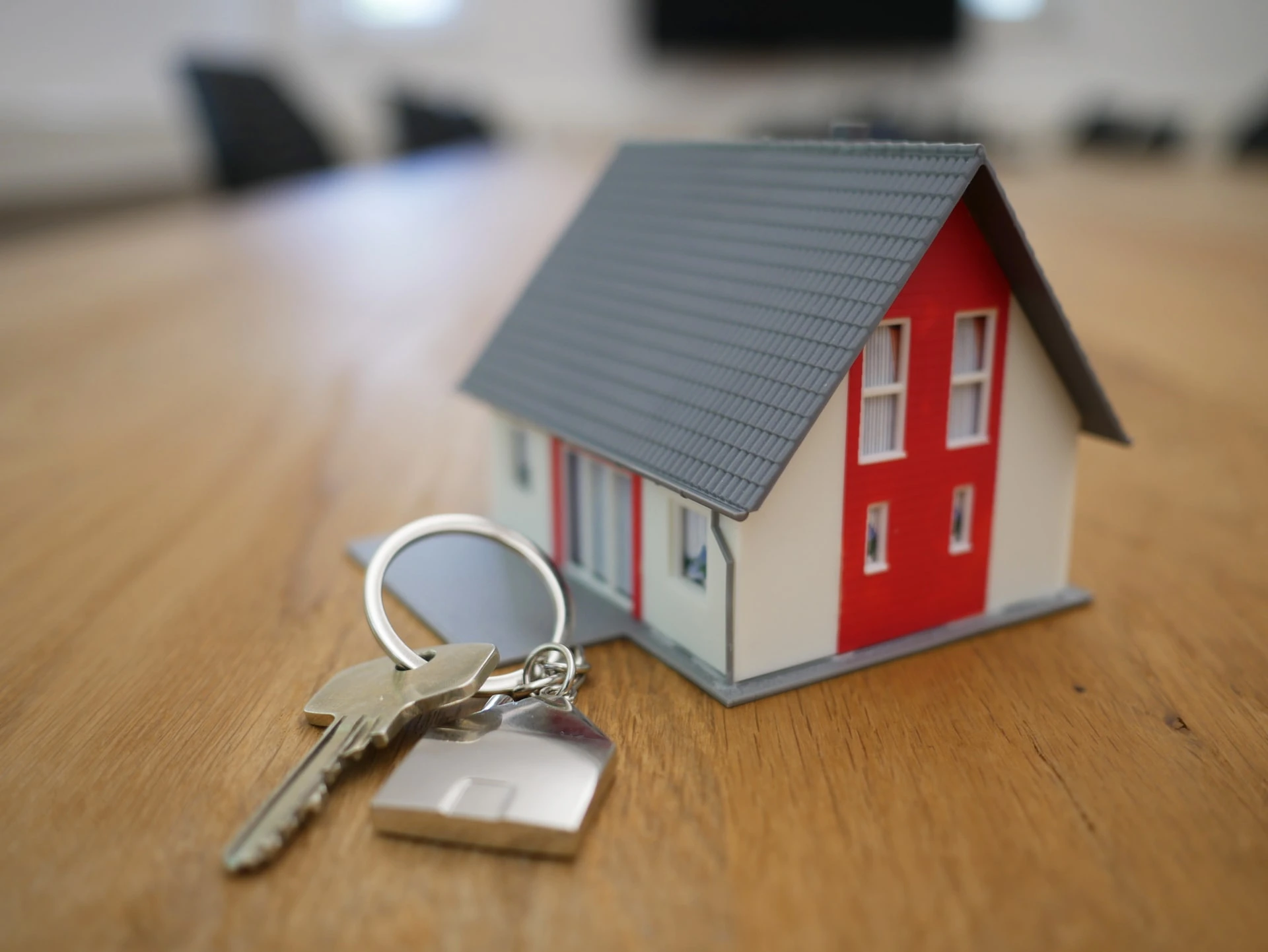 Small house model and front door keys sit on wooden table.