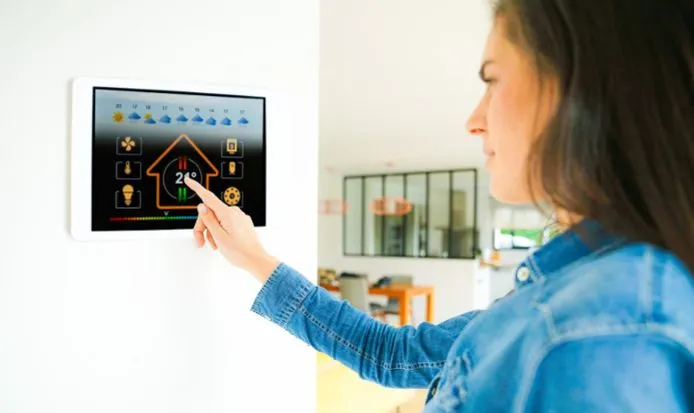 View of a woman setting her smart thermostat at home at a normal temperature because of efficient attic insulation at home.
