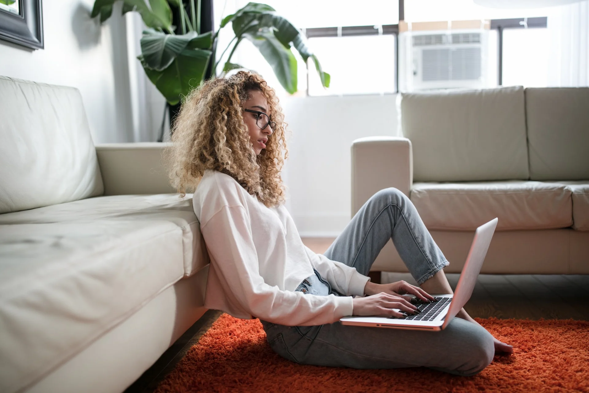 Woman sits on the floor and looks at laptop.
