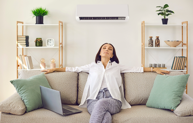 View of a woman relaxing under a wall-mounted air conditioner, enjoying a comfortable indoor environment.