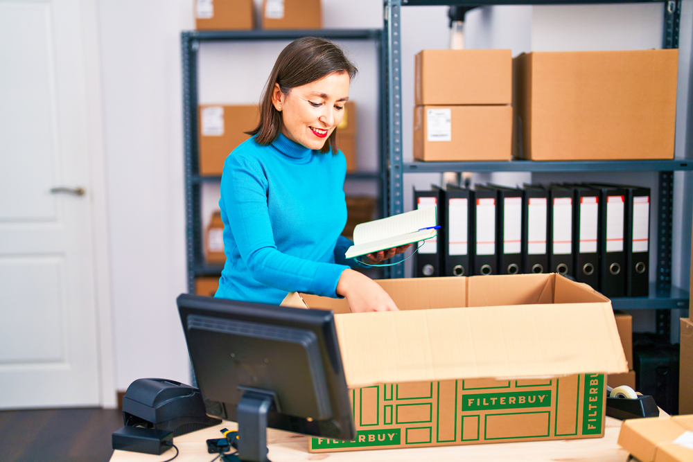 An image of a woman organizing inventory near cardboard boxes, showcasing the importance of keeping storage spaces dust-free.