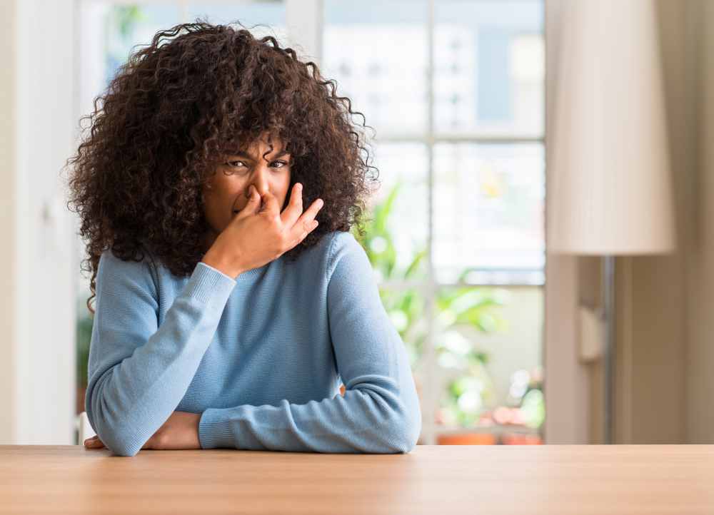 An image of a woman holding her nose due to a bad smell, a common sign that an AC needs immediate repair.