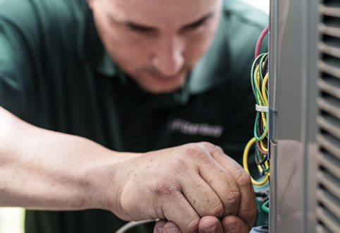 An image of an HVAC technician repairing wiring on a commercial AC unit, showing the qualities of a reliable commercial HVAC repair service near me.