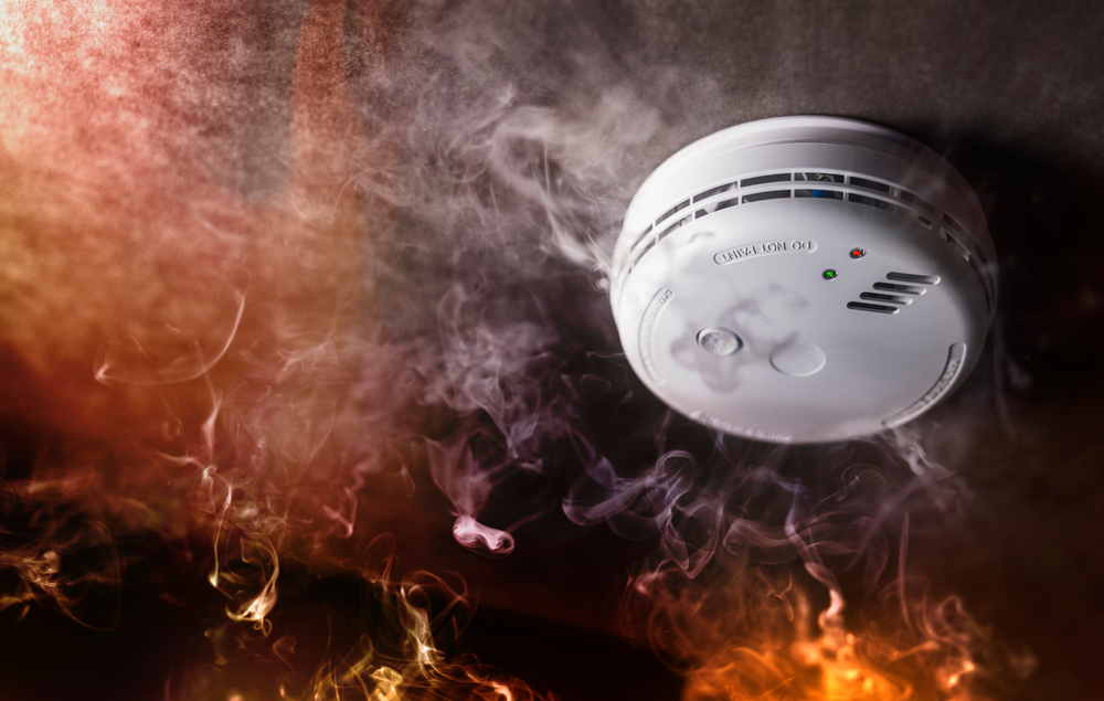 iew of a smoke detector surrounded by smoke, illustrating the danger of clogged dryer vents when cleaning is neglected.