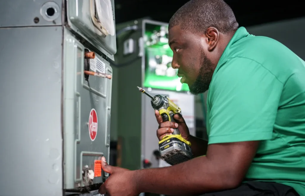 View of an HVAC technician repairing residential furnace using a power drill inside a service area