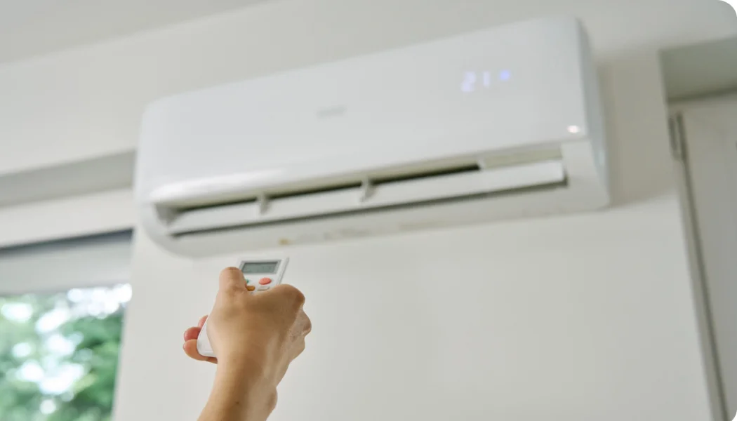 Image of a person using a remote control to operate a wall-mounted air conditioner, showing proper AC use and maintenance for longer lifespan in Florida homes