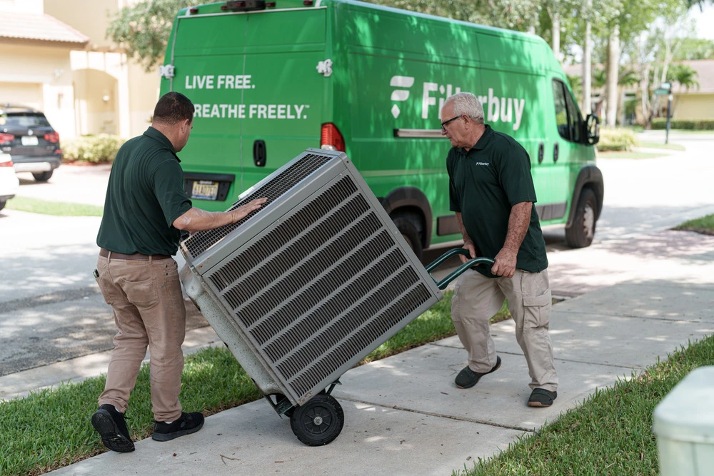 Image of two HVAC technicians installing a new outdoor air conditioning unit at a residential home, representing HVAC system replacement costs and savings.