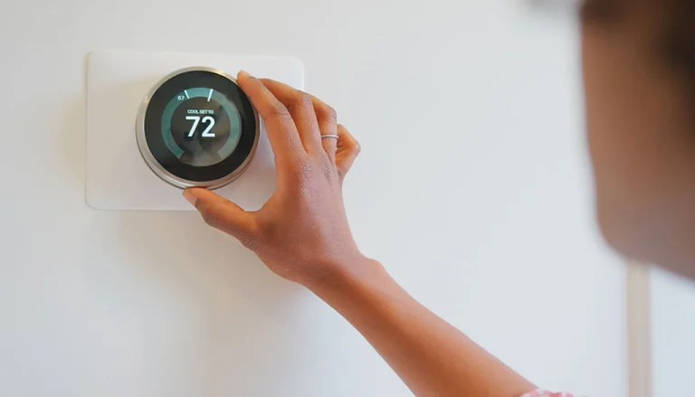 Image of a hand adjusting a smart thermostat set to cooling mode at 74 degrees, illustrating how auxiliary heat functions and thermostat operation.